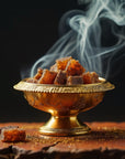Saint O'Niell Alchemy Haute Bohème luxury scented candle of embered spices is conveyed by this golden footed bowl containing cubes of amber emitting whispers of smoke emitting, set against a dark background.