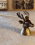 The hand-finished metal Stag's Head Candle Snuffer in an antique gold finish sits atop a natural surface with a backdrop of Renaissance art to convey its natural charm and classic style.