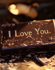 Saint O'Niell Alchemy Grand Cru Chocolat luxury scented candle shows a chocolate bar carved with "I Love You" into it, surrounded by chocolate shavings to depict the seductive quality of the chocolate olfactory pyramid of this exquisitely crafted artisan candle.