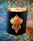 Saint O'Niell Alchemy Joie de Vivre luxury scented candle in a black matte vessel with metallic gold interior set atop a multi-colored Florentine paper design in blues, purples, greens, yellows and reds to convey its Fresh Green olfactory scent pyramid.