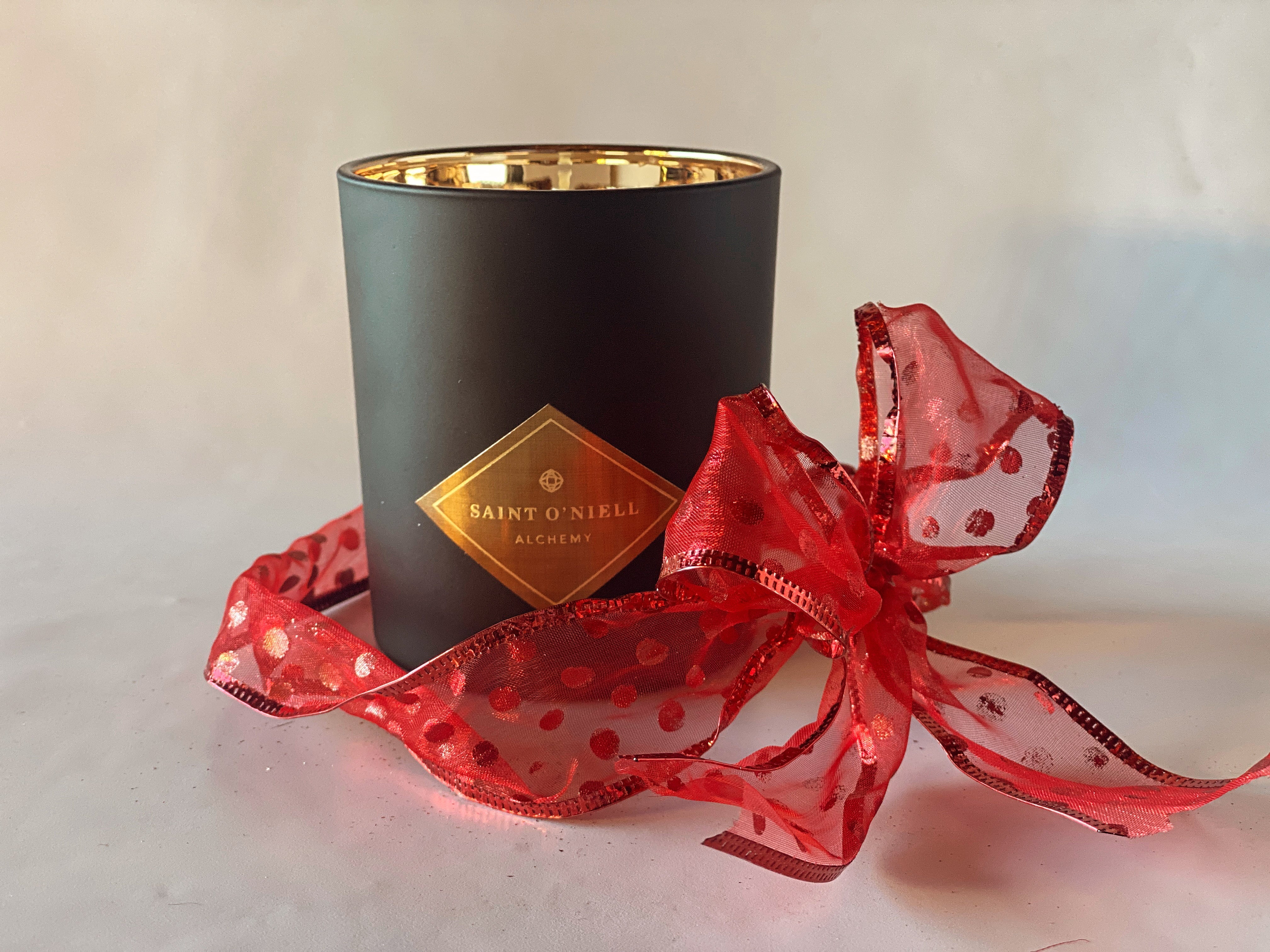 Saint O&#39;Niell Alchemy&#39;s classic luxury scented candle in black matte vessel with gold metallic interior, wrapped in a sheer red dotted organza ribbon, can be purchased via. a Gift Card to allow your people to choose their preferred scent.